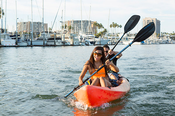 couple rowing in a kayak with boats docked in background