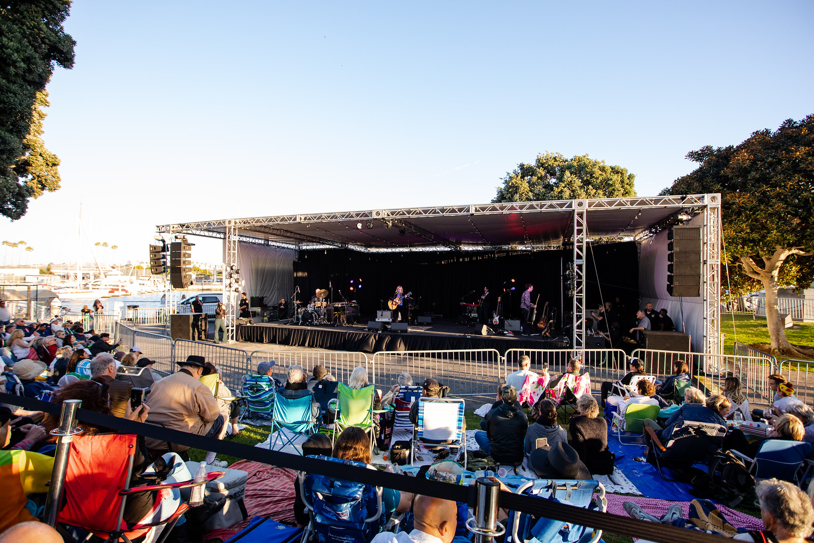 People sitting on lawn in front of stage by the sea during concert at a park