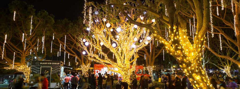 People walking by food trucks and trees in holiday lights